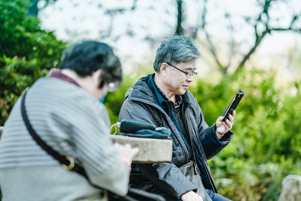 elderly asian couple using smartphones in the park
