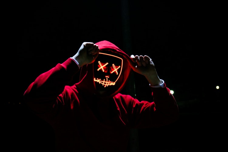 man wearing red hoody representing a hacker with neon light face mask