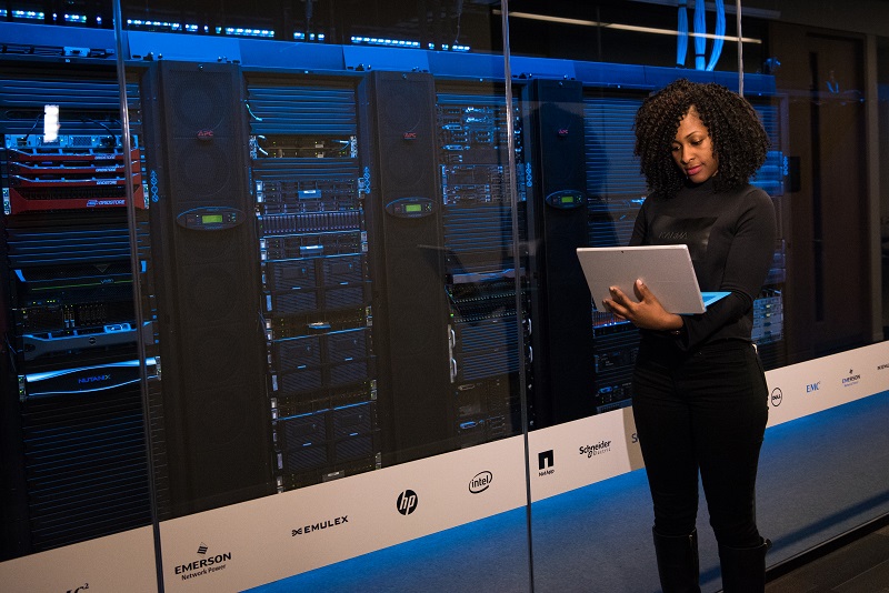 woman standing with laptop in front of physical servers in hosting room